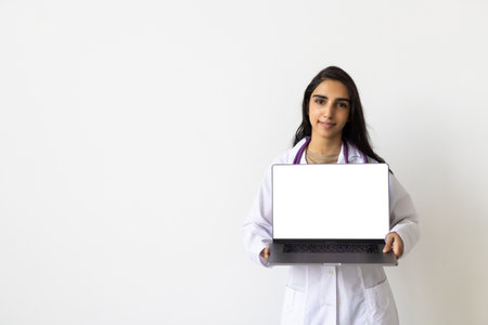 Positive female doctor sitting at desk with laptop.