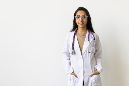 Pretty young smiling clinician in whitecoat crossing arms on chest while looking at you in isolationの写真素材