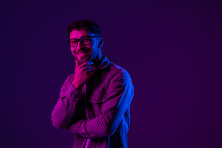 Portrait of calm smiling man in shirt standing with crossed arms, looking at camera with confident facial expression. Indoor studio shot isolated on colorful neon light background.の写真素材