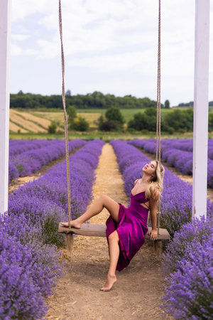 Beautiful free young woman on a swing among bright and fresh lavender on a field. The beauty enjoys her mood and nature.の写真素材
