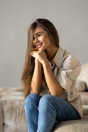 Happy young woman sitting on sofa at home and looking at camera. Portrait of comfortable woman in winter clothes relaxing on armchair. Portrait of beautiful girl smiling and relaxing during autumn.の写真素材
