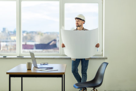 Portrait of a smiling young businessman working on blueprints at the officeの写真素材