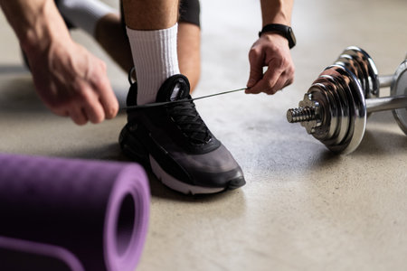Close Up Of Man In Fitness Clothing At Home Fastening Trainers Before Exercising With Hand Weightsの写真素材
