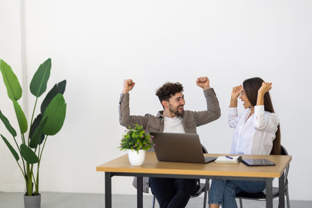 Businesswoman and businessman colleagues celebrate a success with enthusiastic facial expressions looking at the notebook screen.の写真素材