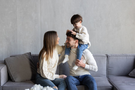 Cheerful family are spending funny time while sitting on the sofa in bright room. Happy parenthood...