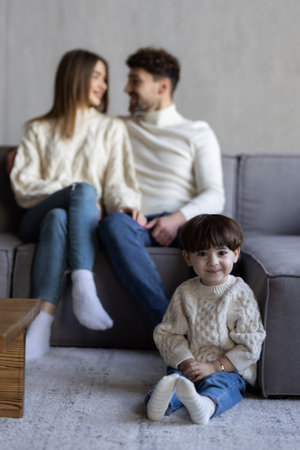 Head shot portrait of happy hispanic couple and preschool son sit on sofa at home smiling looking at...
