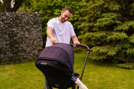family, fatherhood and people concept - happy father with child in stroller walking at summer park