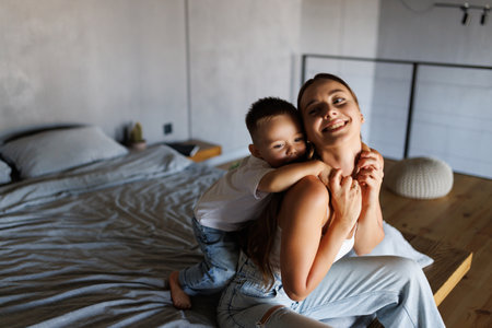 Smiling mom and little son laying on bed at home and hugging.の写真素材