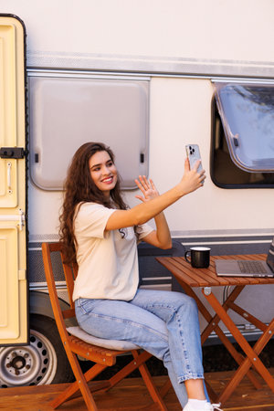 Young pretty woman working on laptop while take selfie on phone while sit at table near table
