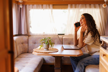 Young woman talking on phone while sitting at table in camperの写真素材