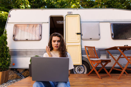 Woman looking at the laptop near the camping. Caravan car Vacation. Family vacation travel, holiday trip in motorhome RV. Wi-fi connection information communication technology.の写真素材