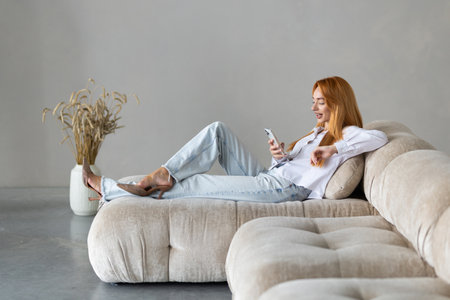 Portrait of woman using a phone and checking email or news online while sitting on sofa at home.の写真素材