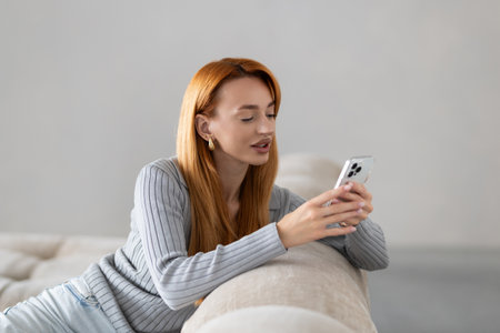 Full body portrait of a happy woman using smart phone lying in the sofa in the living room at night at homeの写真素材