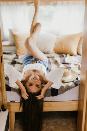 Happy woman sitting on bed inside camper van bedroom and looking outside the window with dreamer expression. Freedom and independence lifeの写真素材