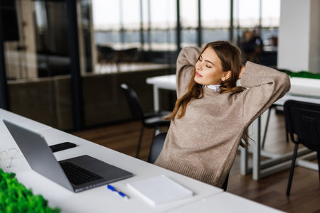 Calm smiling businesswoman relaxing at comfortable office chair hands behind head, happy woman resting in office satisfied after work done, enjoying break with eyes closed, peace of mind, no stressの写真素材