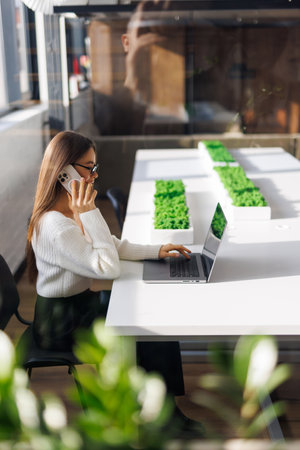 Happy businesswoman talking on mobile phone while analyzing weekly schedule in her notebook.の写真素材