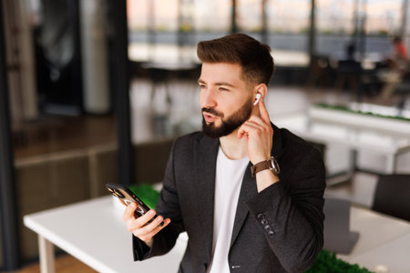 Happy business man at work in home office wearing earbud using cell phone, smiling eastern businessman having virtual mobile chat video call on smartphone, watching game.の写真素材