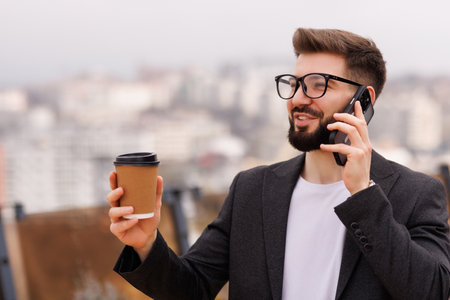 Businessman drinking coffee and using a phone on the terrace of a modern buildingの写真素材
