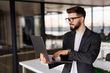 Portrait of handsome businessman smiling while using laptop in officeの写真素材