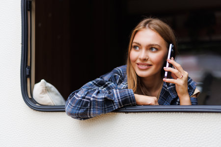 Young pretty woman talking phone while stand in front of motorhome