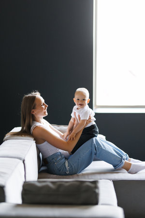 Mother lifts the baby up in her arms, sitting on the bed and entertaining him