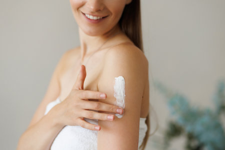 Beautiful young woman with towel wrapped around her head applying face mask at the bathroomの写真素材