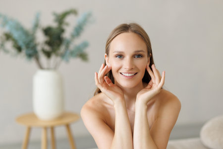 Skin care. Woman with beauty face touching healthy facial skin portrait. Beautiful smiling girl model with natural makeup touching glowing hydrated skin on white background closeupの写真素材