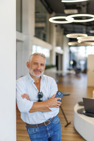 Smiling busy professional business man standing in office holding mobile cellphone. Young happy...