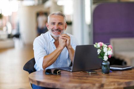Mature Businessman Wearing Glasses Working On Laptop At Desk In Officeの写真素材