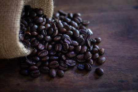 close up coffee beans in sack on wooden table background . black and brown color seeds textured .の写真素材