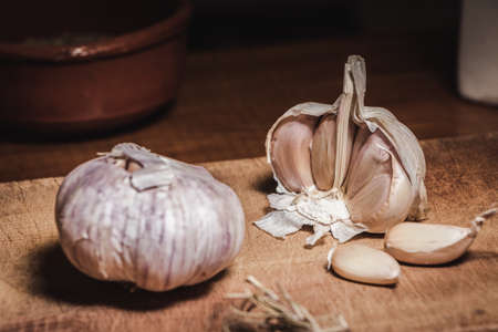 Garlic head and cloves on wooden board next to rosemary branches on rustic tableの写真素材
