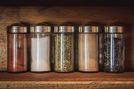 Jars with spices: paprika, oregano, salt, chia, sesame on wooden shelfの写真素材