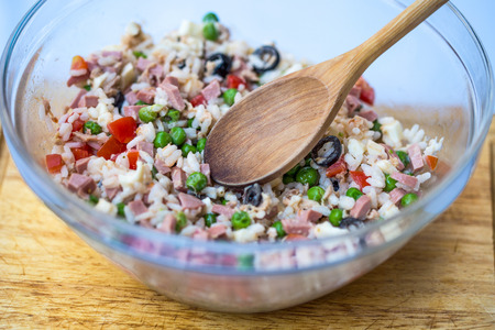 Italian rice salad or cold rice in a glass case with woodden spoon on a chopping board with white background.の写真素材