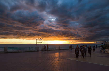 GENOA, ITALY, FEBRUARY 7, 2020 - People walking on the Genoa promenade under a cloudy sky at sunset,  Italyのeditorial素材