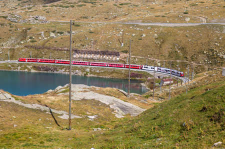 The typical red Bernina Express train at Bernina Pass between Italy and Switzerland in summertime.