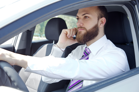 Serious young executive man with tie and white shirt in car on the phone