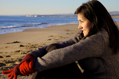 smiling woman looking at the horizon sitting on a beach in front of the oceanの写真素材