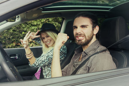 Young couple in his car, happy to drive on a country road, focus on the man