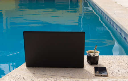 Notebook, mate and cell phone by the pool.の写真素材