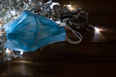 Christmas in times of coronavirus. Surgical mask over christmas lights in the dark. Covid-19の写真素材