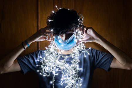 Young man with surgical mask, Christmas lights around. Christmas in times of coronavirus.