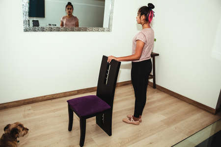 Teen girl at home looking at herself in the mirror, ready to practice ballet and gymnastics while her dog watches herの写真素材