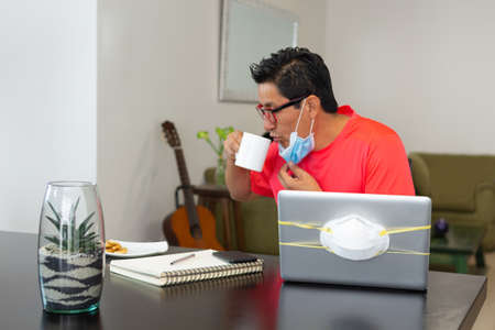 A man lowers his coffee mask while working at home due to covid-19 quarantine