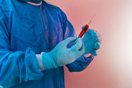 Doctor with gloves and protective equipment prepares a syringe with red medicineの写真素材