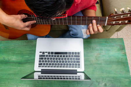 Aerial shot of a man who receives online guitar lessons at home during his quarantineの写真素材