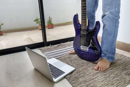 Electric guitar online class. Detail of legs with bare feet on a mat at home in front of the computerの写真素材
