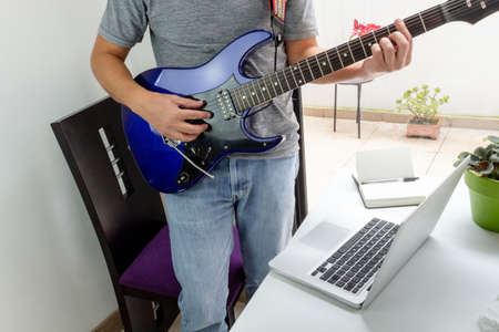 Shot of a man whose face is not seen taking electric guitar classes online at home. Activities during quarantineの写真素材