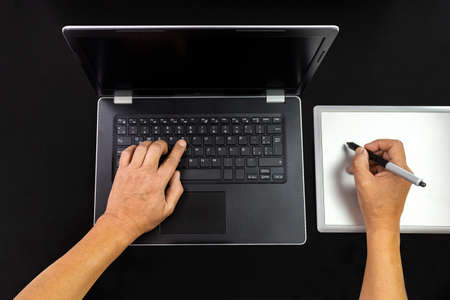 Hands working on a black computer isolated on black background with a graphic tablet
