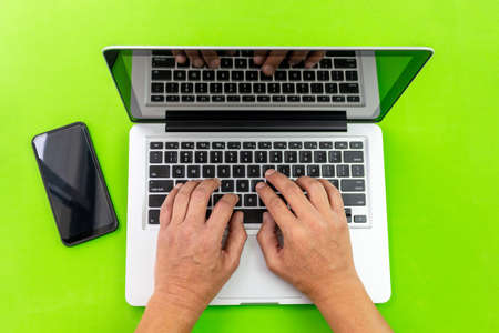 Shot from above of some hands on a computer and a cell phone isolated on green chroma background with pathの写真素材