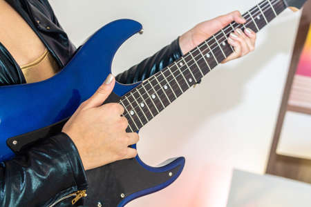 Close-up of the hands of a teenage girl playing the electric guitar in...